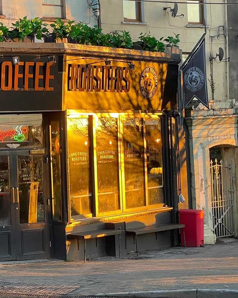 A Cork Coffee Roasters café front in the evening: a dark front with gold-lit windows.