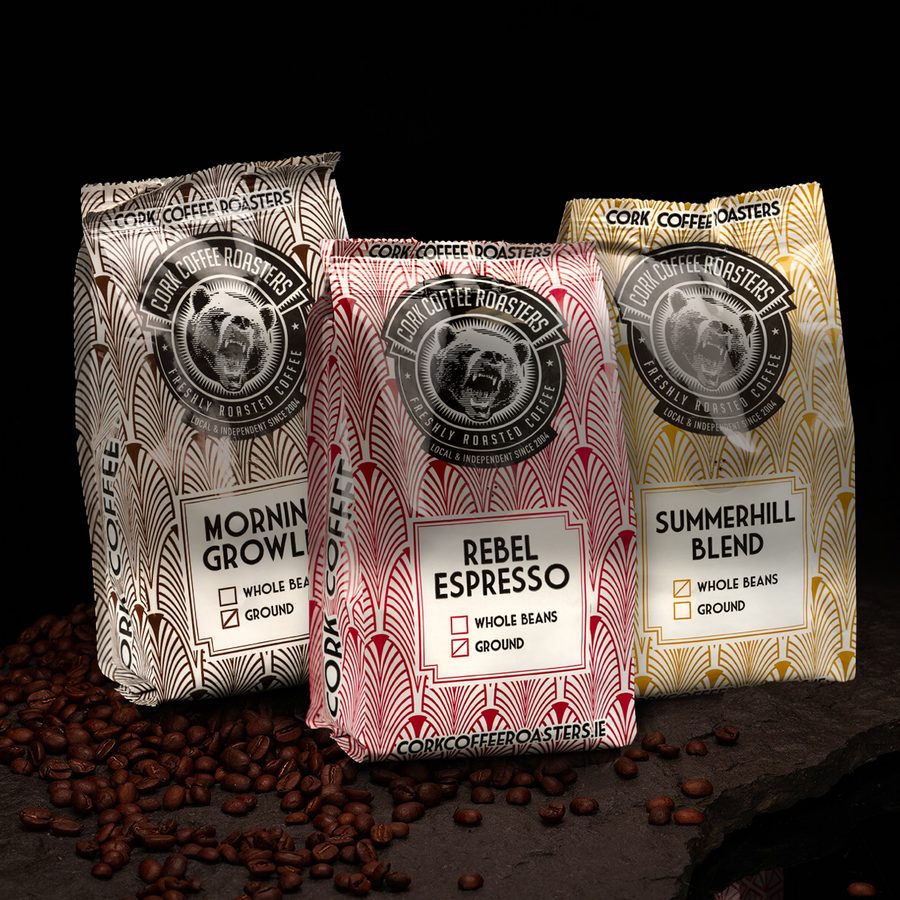 Three retail bags of coffee on a stone slab with loose beans.