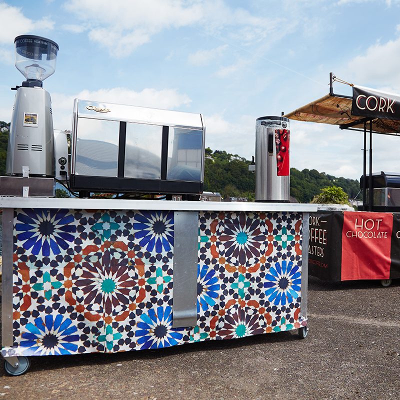 A mosaic-tile espresso cart with grinder and machine on the harbour front.