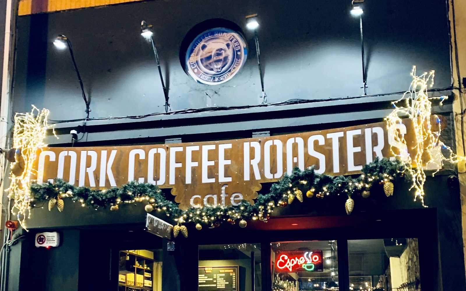 The Anglesea Street frontage at night: a dark front, the bear roundel above a rust-coloured Cork Coffee Roasters sign, lit by Christmas lights.