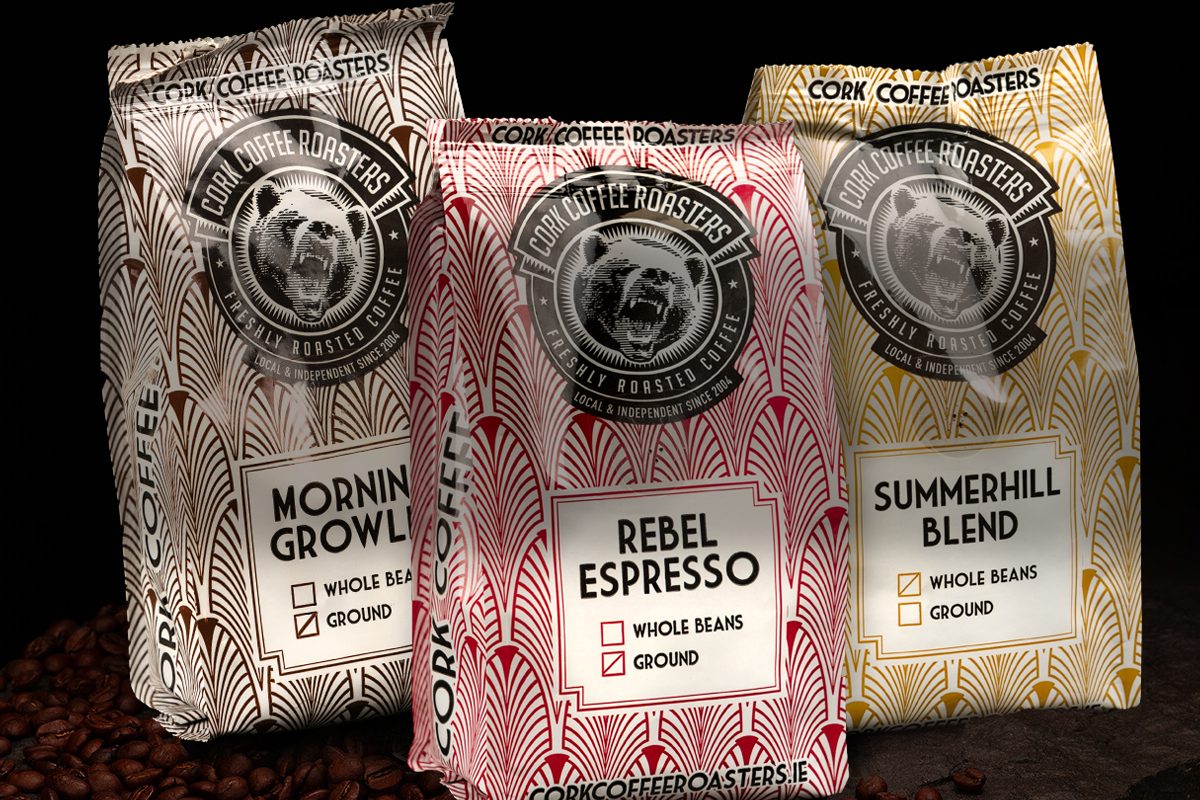 Three bags of Cork Coffee Roasters coffee, Morning Growler, Rebel Espresso and Summerhill Blend, on scattered beans.